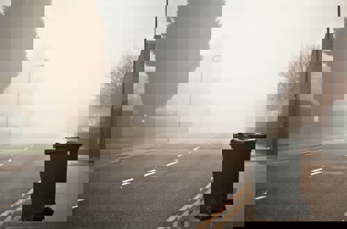 black wheelie bin by roadside on foggy day