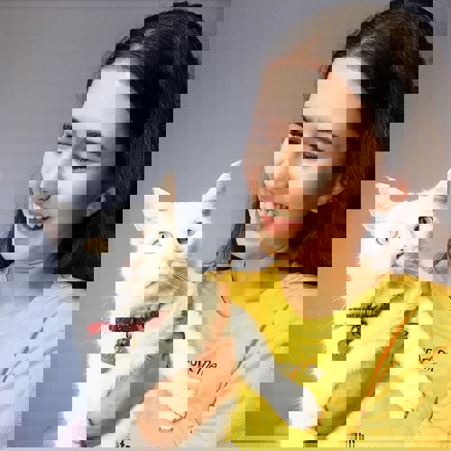 Brunette woman wearing yellow t-shirt and holding white cat with red collar